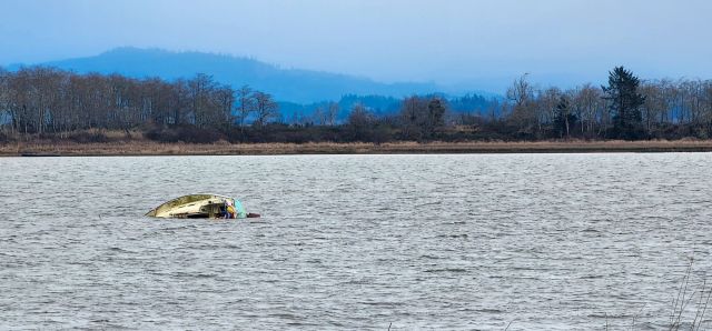 a color photo of half a sailboat in a wide expanse of salt water. There are blue hills, blue trees and a gray blue sky in the distance.