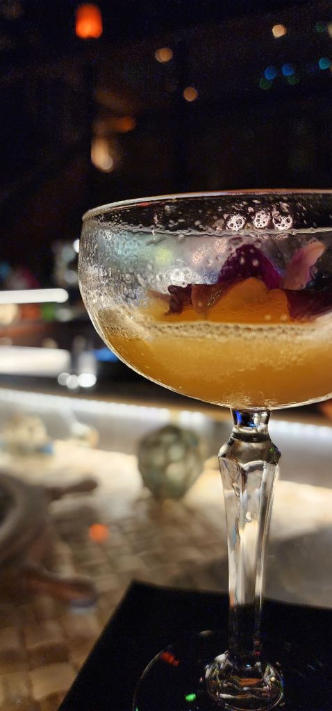 a closeup photo of an orange cocktail in a rounded martini glass
