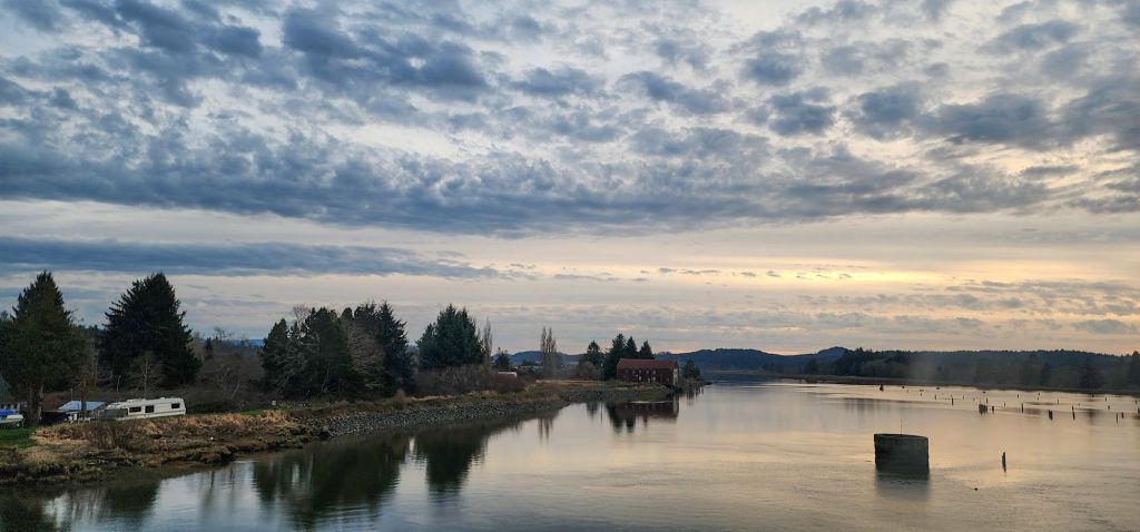 A watery landscape of a river reflecting the cloudy twilight sky and trees on the bank