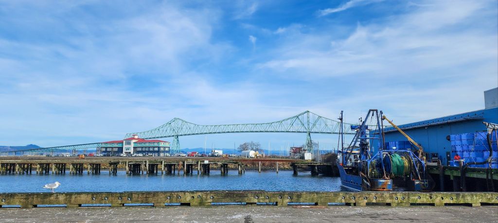 A picturesque scene of the Astoria waterfront with a view of the Megler bridge and a crab boat in the foreground