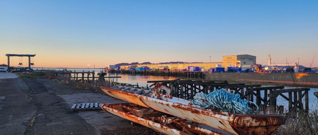 a rusted float in the foreground of a sunset photo of the Port of Astoria