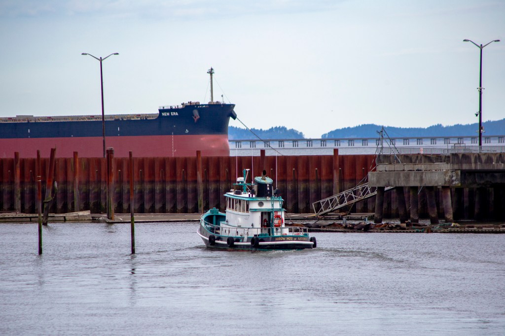 a photo of a small boat in a harbor blocked of by a metal sea wall. There are sea lions in front of the wall and a huge cargo ship called the New Era behind it.