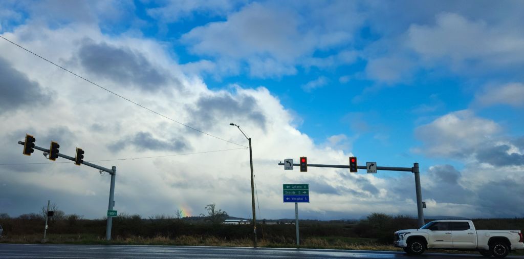a photo of an intersection; in the distance is part of a vivid rainbow
