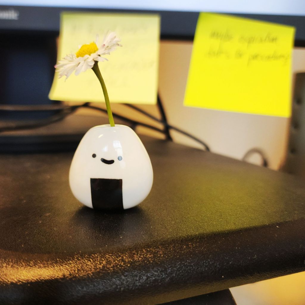 A color photo of a tiny flower in a tiny white holder with a face on it