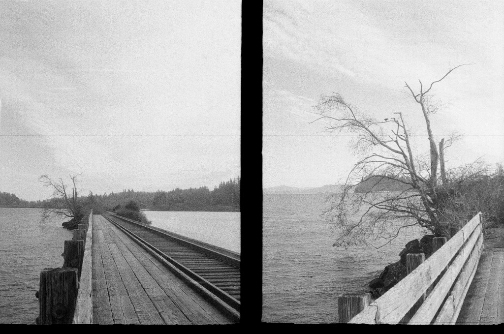 2 black and white photos of a wooden walkway on piers in the water with a railroad track alongside