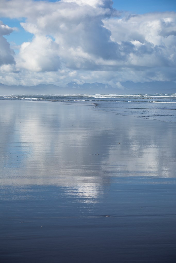 a view of the beach; clouds in the sky are reflected in the wet sand below